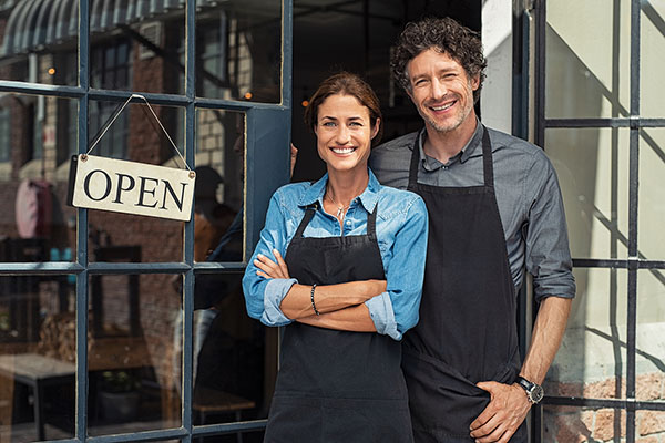 two-cheerful-small-business-owners-posing-next-to-open-sign